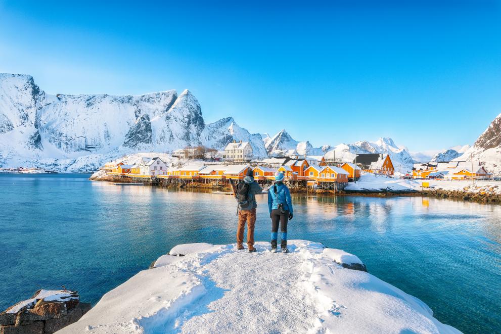 Сouple of tourists admire the view of the Sakrisoy village and snowy mountaines on background.