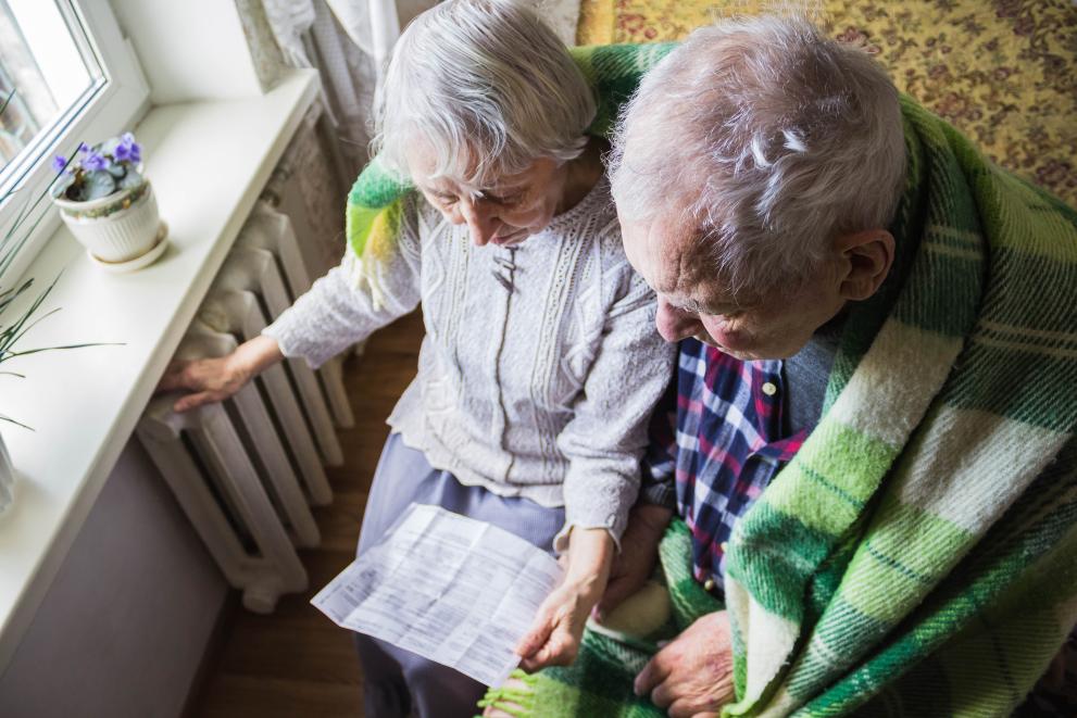  Elderly couple near a radiator looking at an energy bill while under a blanket for warmth