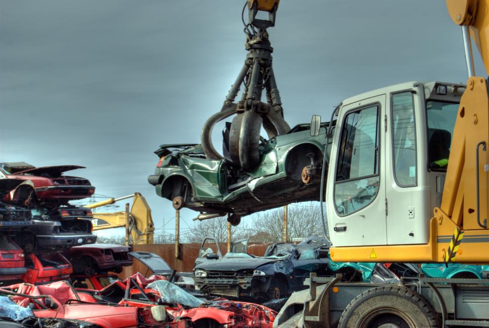 a car wreck, lifted by a machine from a scrapyard, ready to be stored on a pile of vehicules