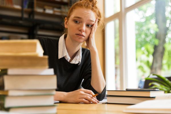 An anxious student looks at a pile of books to be studied