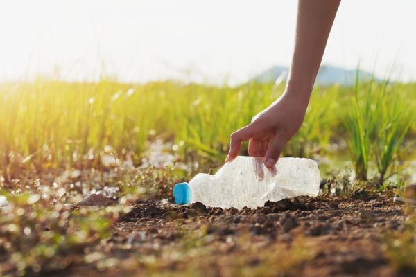 Someone picks up a plastic bottle on a path bordered by fields
